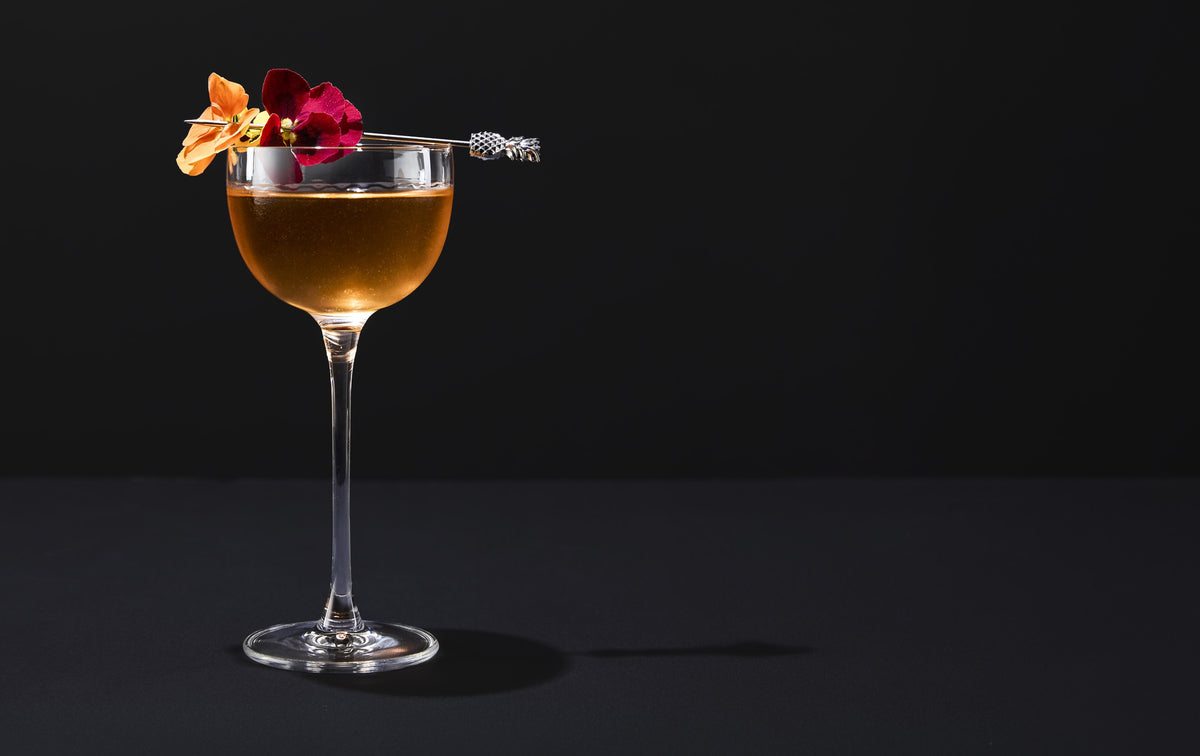 Hertini in a stemmed glass with orange and red edible flowers on a pick